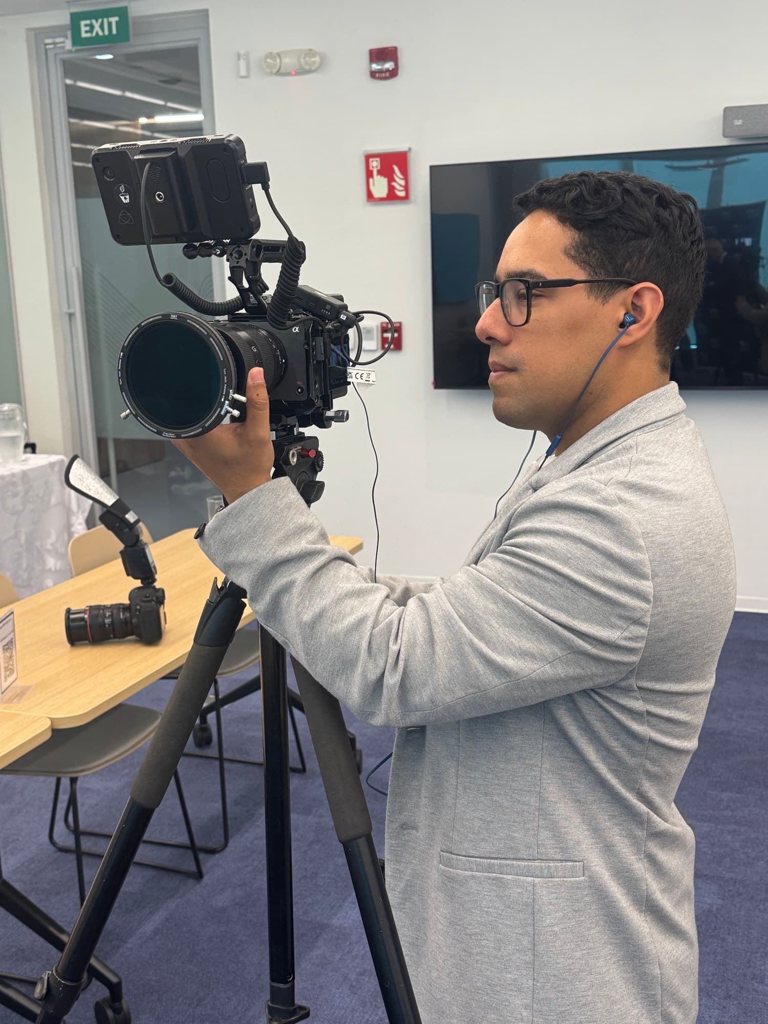 Andrés López operating a cinema camera on a tripod during an indoor corporate shoot