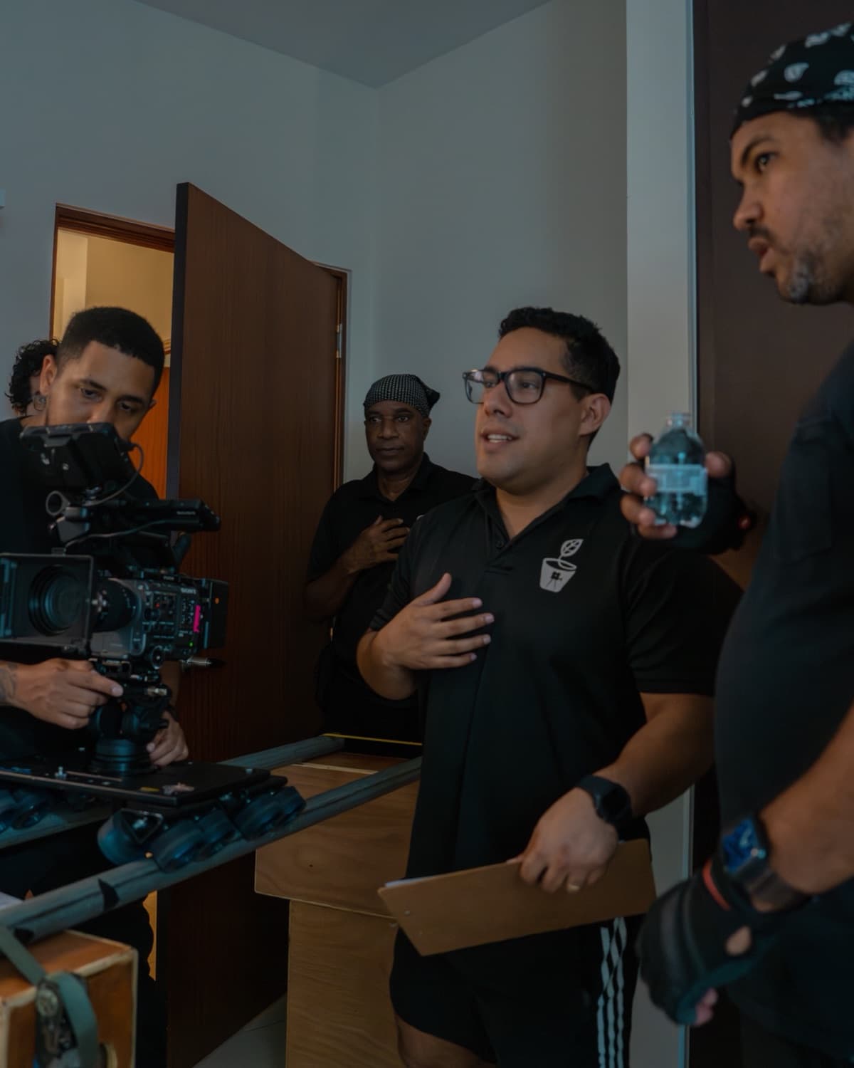 Andrés López directing his crew on an indoor set, next to a camera operator on a dolly, lights and a clapperboard